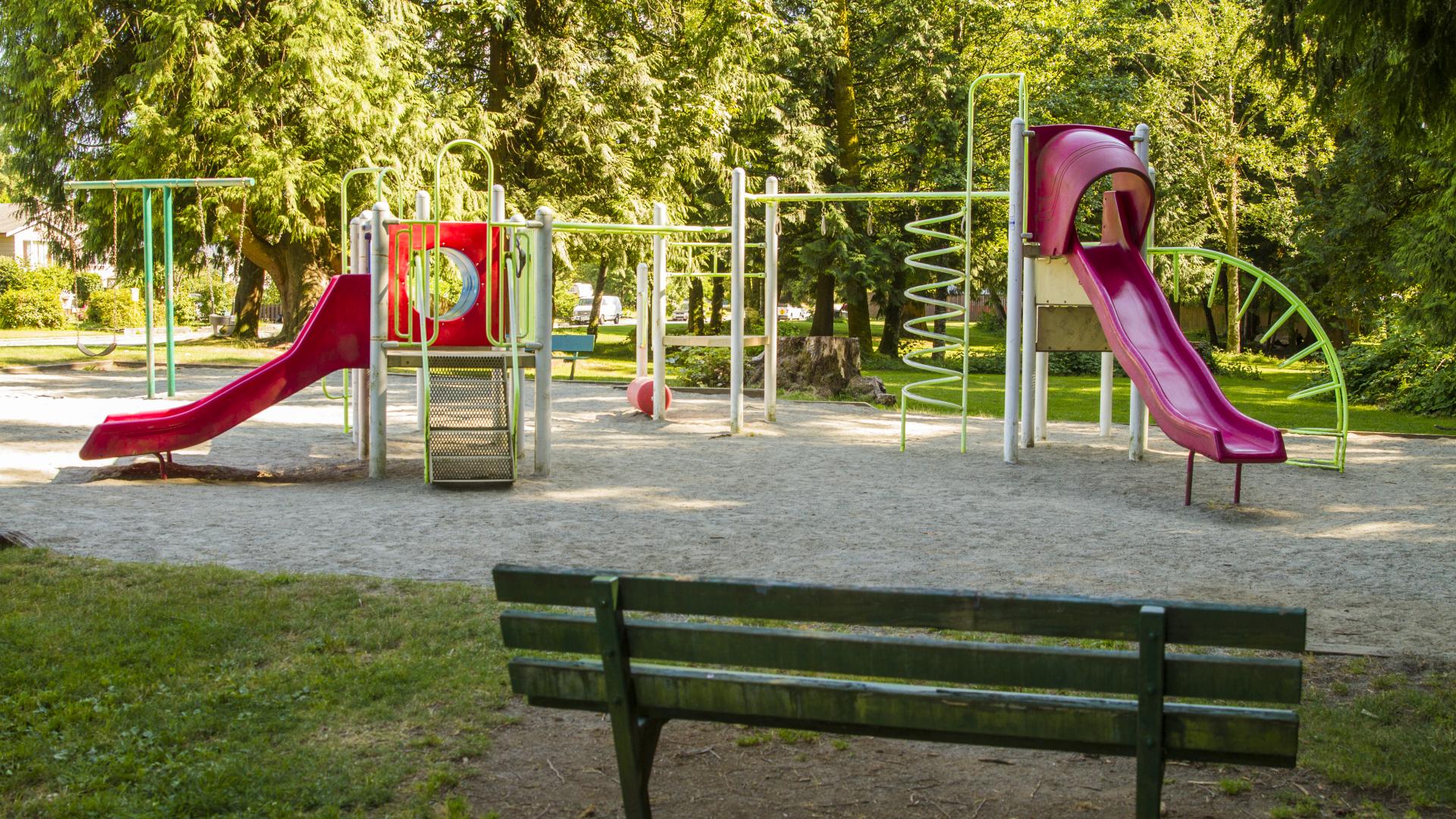A red and green playground with a small bench in the grass nearby.